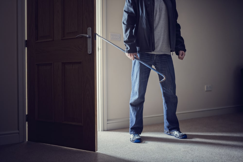 Person Standing With A Crowbar Next To An Opened Door